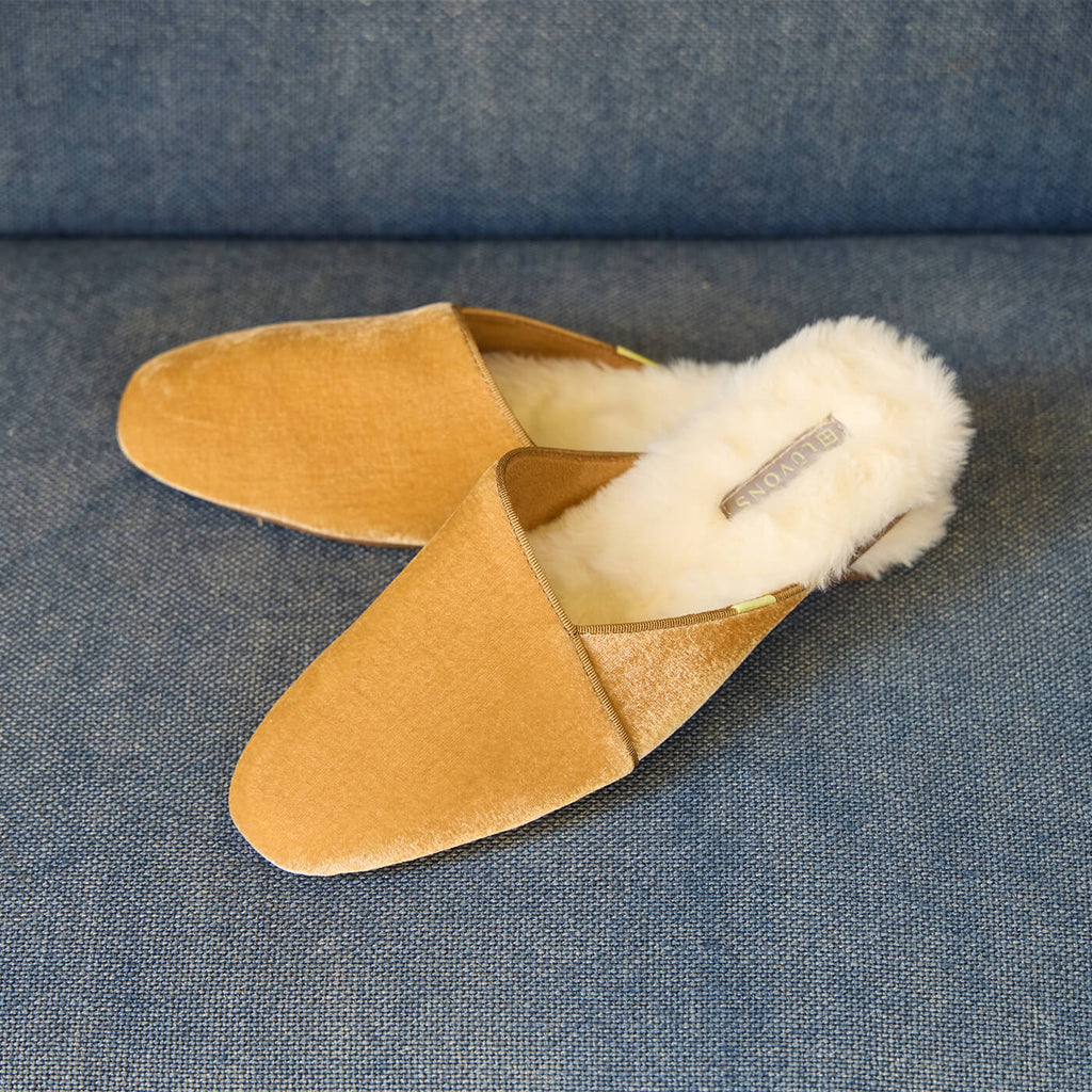 Luvons Devon slippers in camel velvet with plush shearling lining, resting on a blue fabric sofa—stylish, supportive, and machine-washable.